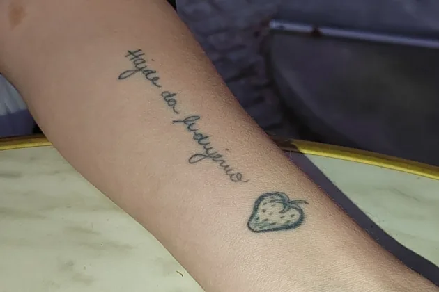 Wrist with a tattoo reading 'Hajde da ludujemo' with a strawberry next to it.