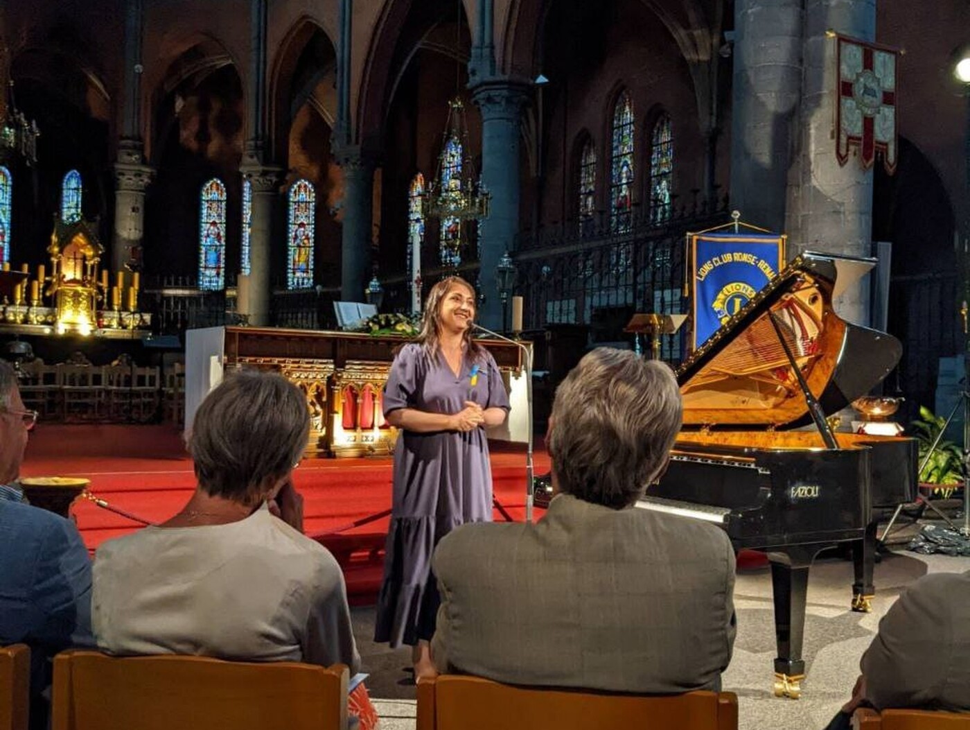 Natalya stands in front of an audience at an event taking place in a church. She is speaking into a microphone.
